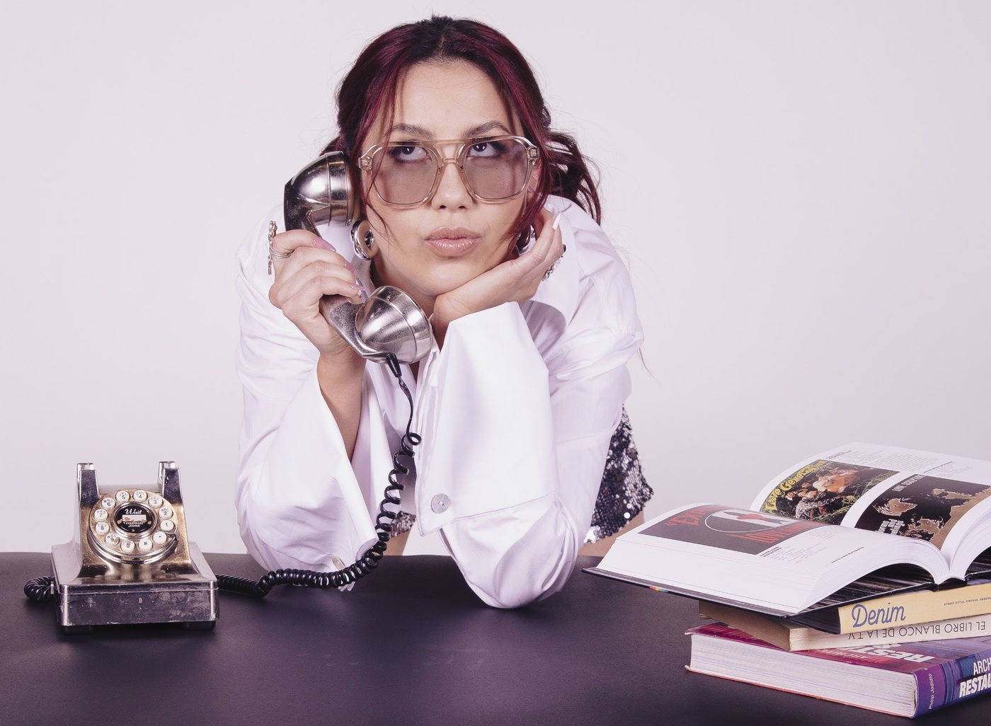 Carolina Hernández en su escritorio, con gafas y un teléfono retro, entre libros